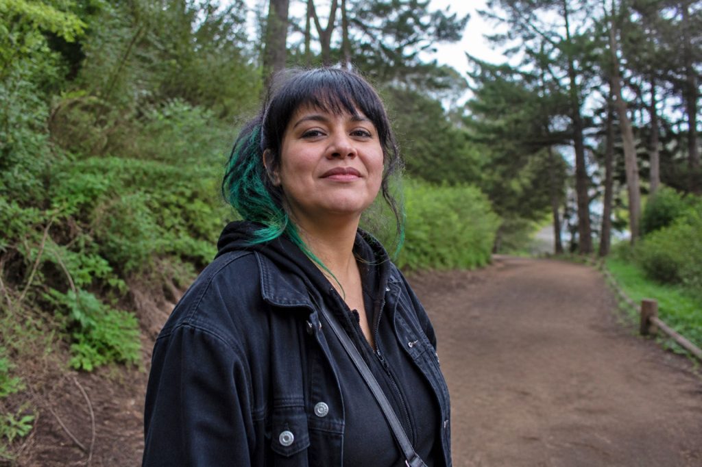 A woman in a dark jacket and green highlighted hair smiles